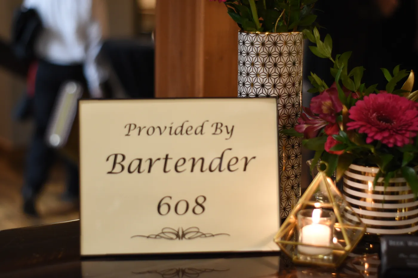 Provided By Bartender 608 sign on a candlelit bar