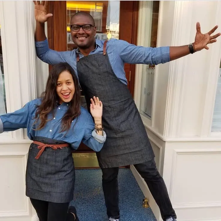 Two Bartender 608 team members in denim aprons, arms wide