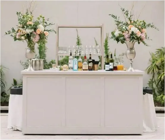 A white bar with floral arrangements and a curated spirits lineup